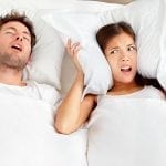 Couple in bed, man snoring and woman can not sleep, covering ears with pillow for snore noise.