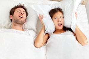 Couple in bed, man snoring and woman can not sleep, covering ears with pillow for snore noise.